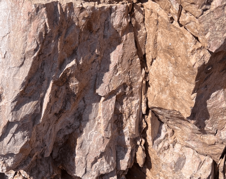 Talc Powder and Feldspar Company - Close-up of rough, fractured pink feldspar rock face with varied textures and shadows.